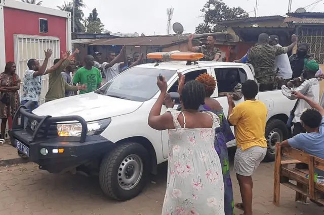 Soldiers wave from the back of a moving pickup truck as residents of Libreville stand by and applaud