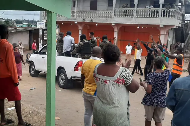 A moving pickup truck carrying soldiers through Libreville is pictured from behind, as people stand and applaud