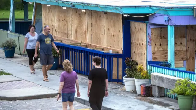 People walking near a building covered with plywood as the town prepares for Hurricane Idalia in Cedar Key, Florida, USA, 29 August 2023