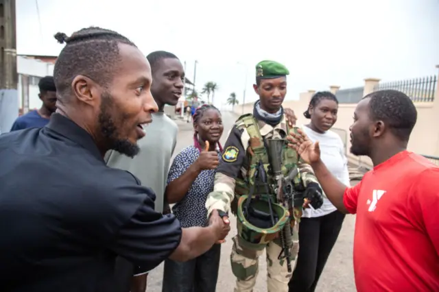 A group of men greet and shake hands with a member of Gabon's presidential guard