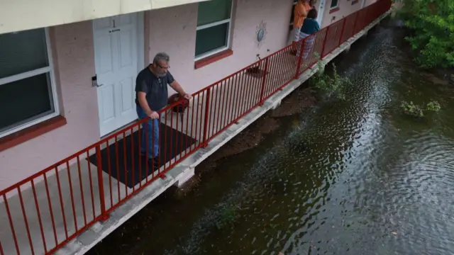 A man stands on a balcony, looking over floodwater