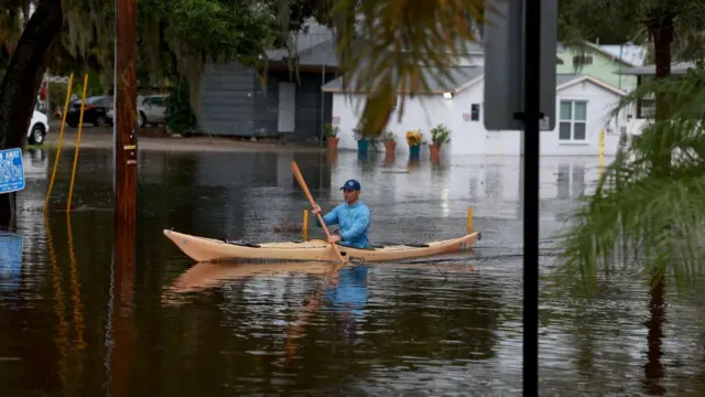 A man in a blue shirt kayaks through a flooded intersection