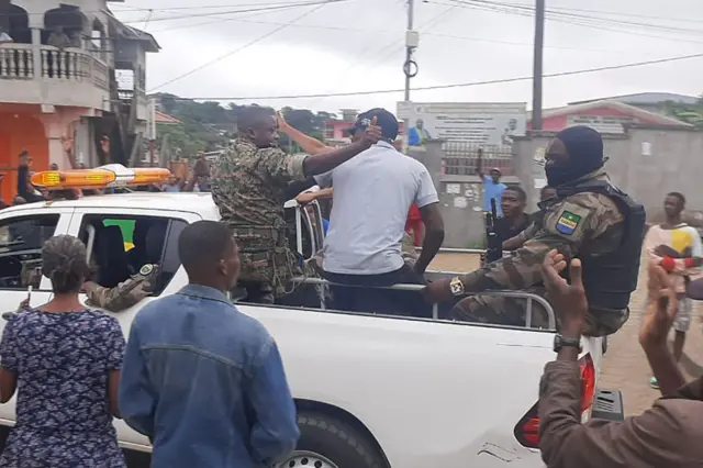 Soldiers give thumbs-up signs from the back of a moving pickup truck as residents of Libreville stand by and applaud