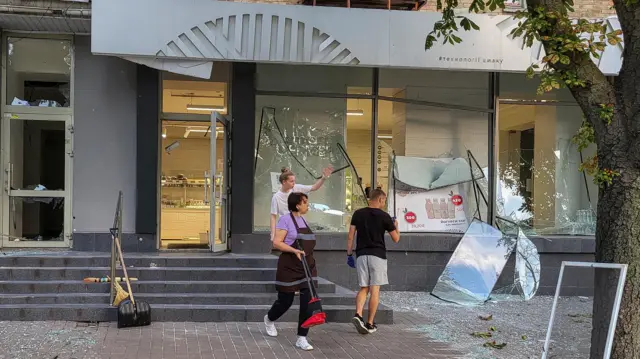 Staff clean up broken windows of a store damaged during a missile strike in Kyiv