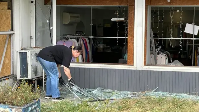 A woman in black gloves picks up broken glass