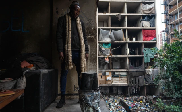 A man stands next to a makeshift heater near the opening in the wall of a "hijacked" building in Johannesburg