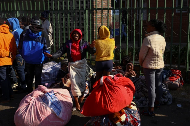 A woman screams as residents stand near a fence with their belongings