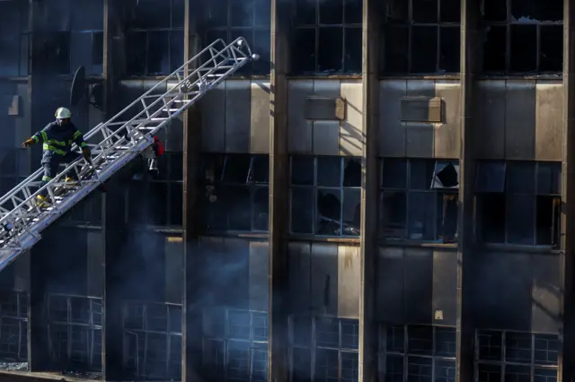 A firefighter on a ladder near the burned building