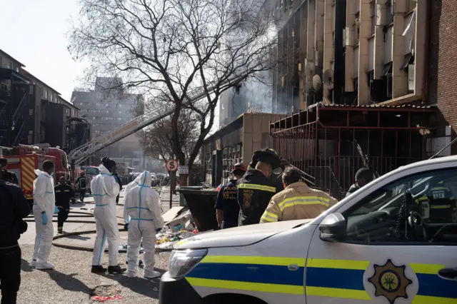 Rescue workers and an emergency services vehicle outside the burned building