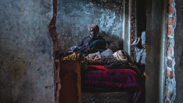 A person seen through a hole in the wall sits among fabrics and blankets in a "hijacked" building in Johannesburg