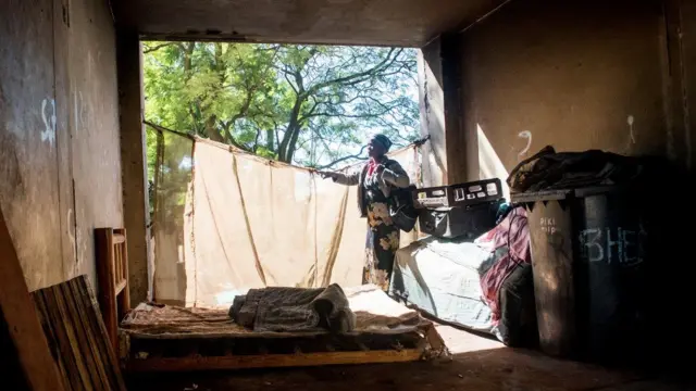 A woman holds a rod with a piece of fabric attached to it to cover a massive hole in Johannesburg's "hijacked" building