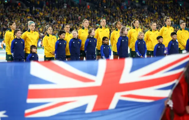 Australia players sing the national anthem with the flag in the foreground.