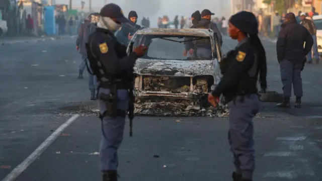 Members of the South African police stand near a burnt-out vehicle in Nyanga during the ongoing strike by taxi operators over a number of grievances against traffic authorities in Cape Town, South Africa, August 7, 2023