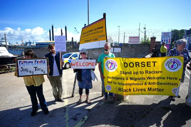 People hold up signs supporting asylum seekers, saying "welcome" and "respect refugee lives" in Dorset