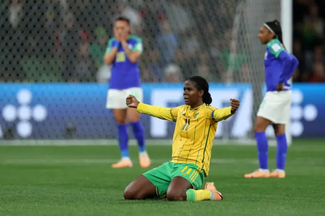 Jamaica forward Bunny Shaw celebrates on her knees on the pitch as they qualify for the next round.