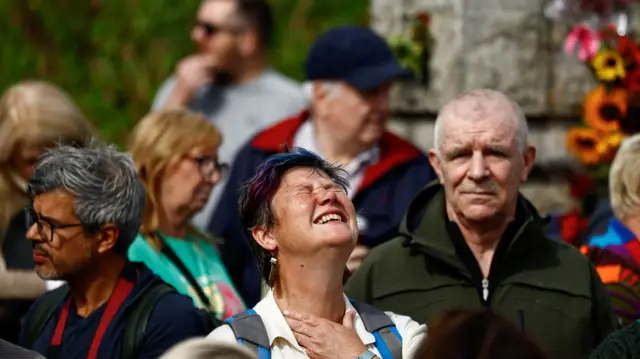 A woman cries, with her hand on her chest, after seeing the hearse carrying O'Connor