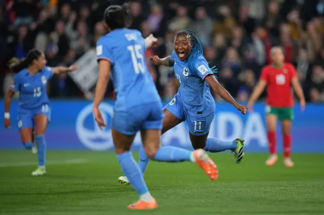 Diani stretches her arms wide as she runs off to celebrate to her teammate in the foreground.