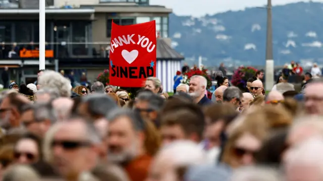 Someone holds a sign saying "thank you Sinead"