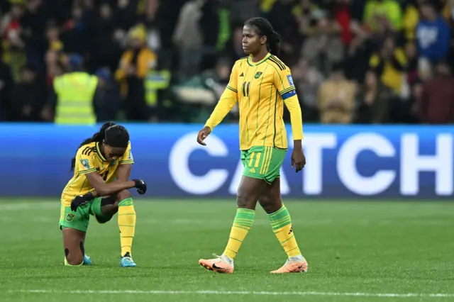 Jamaica players stand stunned after their defeat, one player is knelt down on the floor.