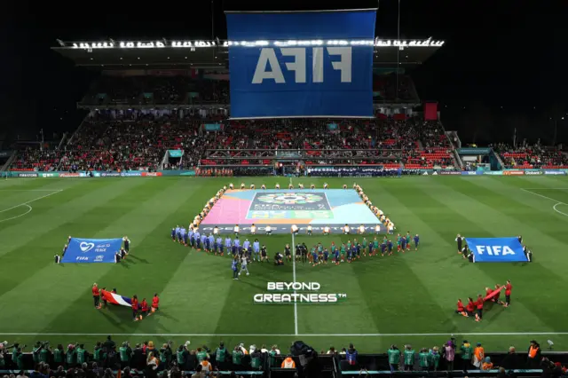 The players stand ready on the field for the national anthems.