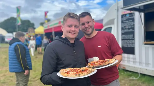 Dau ddyn ar faes yr eisteddfod yn dal pitsas