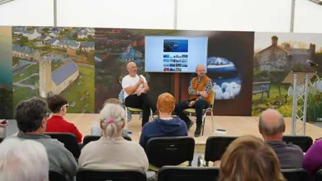Dau ddyn yn trafod teithiau cerdded ar faes yr Eisteddfod