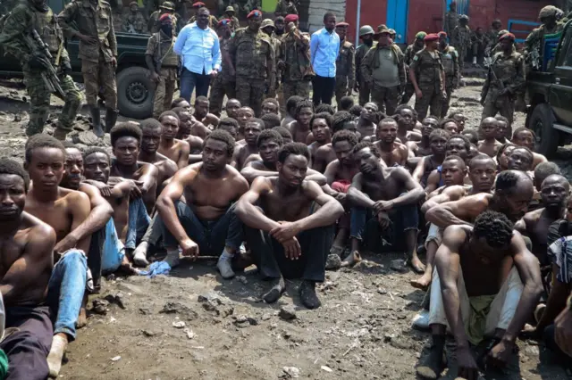 People arrested during a military operation to prevent a planned demonstration against the United Nations by a religious sect, sit on the ground and guarded by the army in Goma, eastern Democratic Republic of Congo on August 30, 2023.