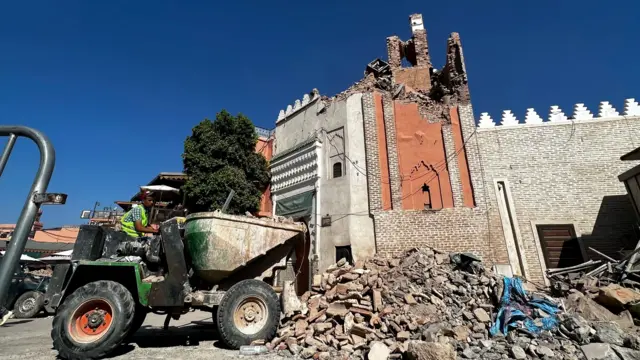 A construction vehicle cleaning up rubble next to the collapsed minaret of the Jemaa el-Fnaa mosque