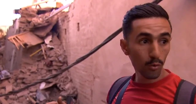 Youssef At Ali standing in front of a narrow alleyway filled with rubble