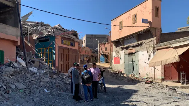 Residents stand in the midst of rubble and damaged buildings