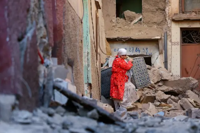 A woman carries belongings out of a damaged building, in the aftermath of a deadly earthquake in Moulay Brahim, Morocco, September 10, 2023