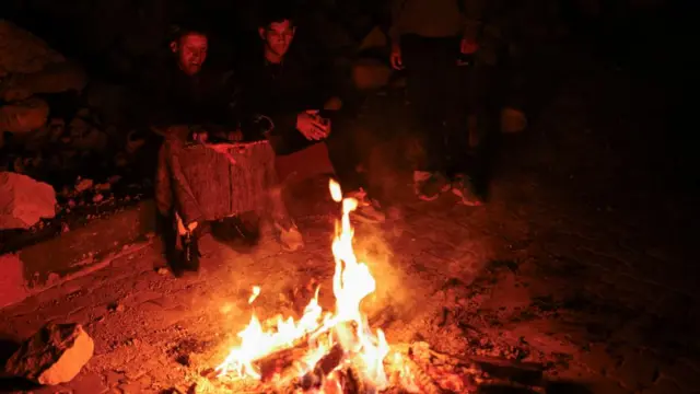 People sit by a bonfire lit in the street