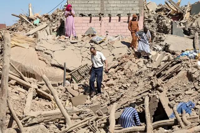 People clamber over rubble and debris, inspecting the ground for signs of life