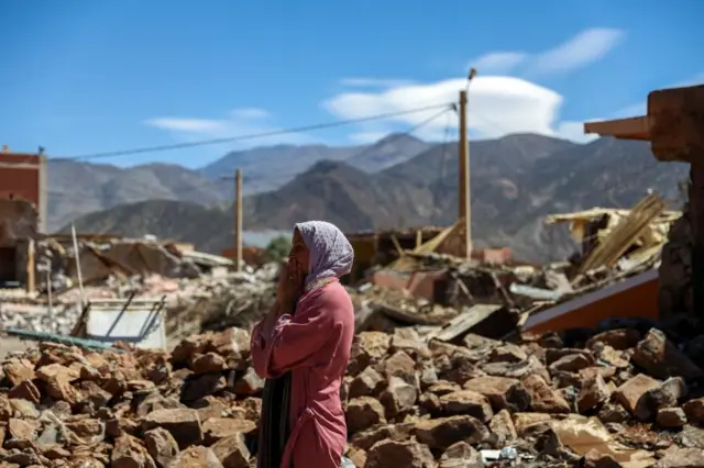 A woman watches near the rubble of a building