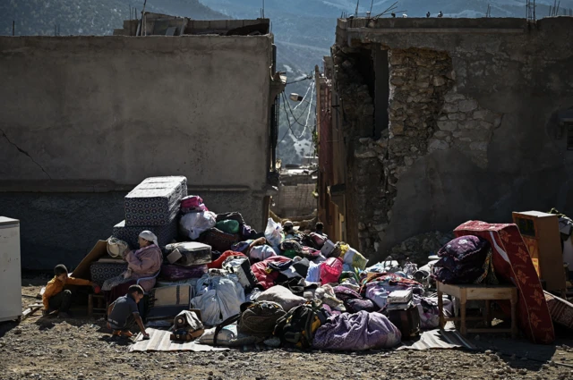 A family sits next to their belongings after their home was destroyed following an earthquake in the mountain village of Moulay Brahim