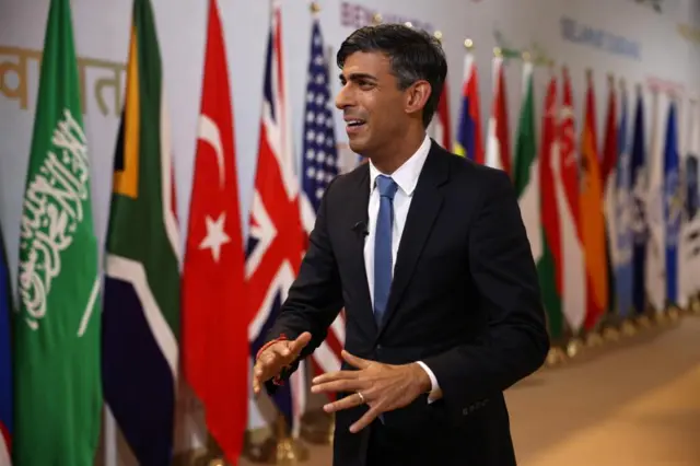 Rishi Sunak speaking to reporters at the G20 in India last week, standing in front of a long line of flags from around the world