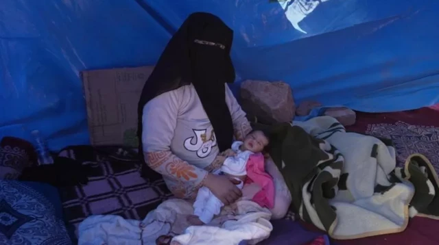 Khadija holds her baby in a tent by the side of the road in Asni, in the Atlas ranges