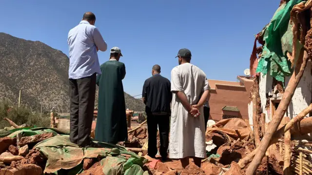 Four men standing amid rubble