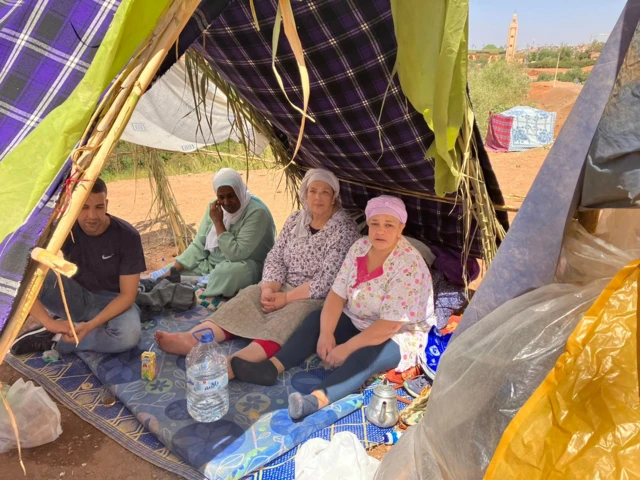 A man and three women sit under a makeshift tent