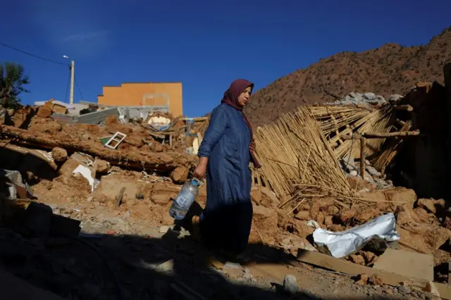 A woman carries a bottle as she walks past a building which has been destroyed by the earthquake