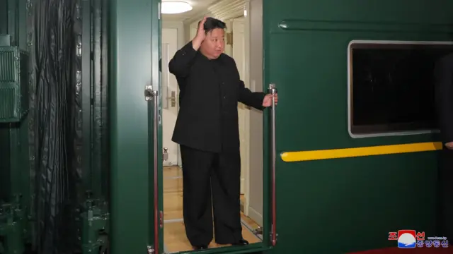 Kim Jong Un waves from a green train as he departs Pyongyang, North Korea