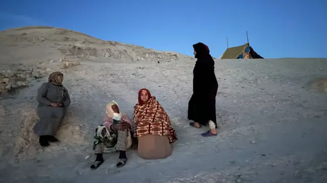 Hakima, wrapped in a patterned blanket, on bare hillside