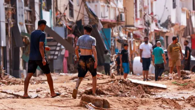 Two men caked in mud walk down a street littered with debris