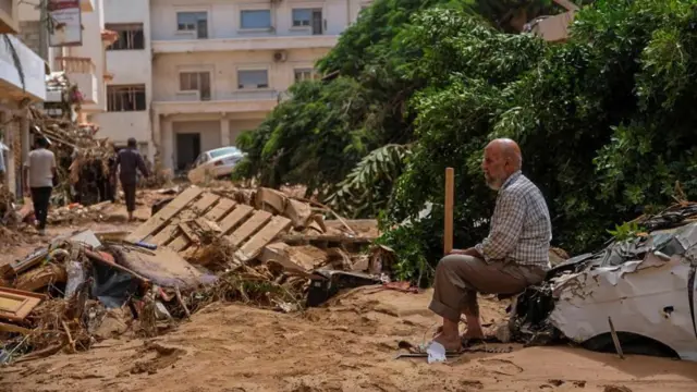 A man sits on the bonnet of a destroyed car amongst debris