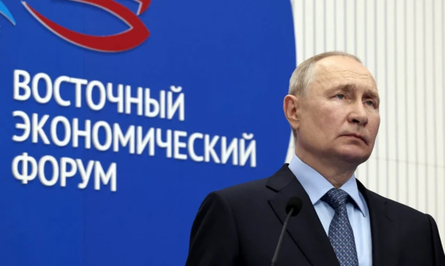 Putin stands in front of a sign reading Eastern Economic Forum