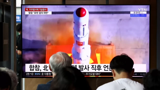 Two people watch a space launch on TV in North Korea