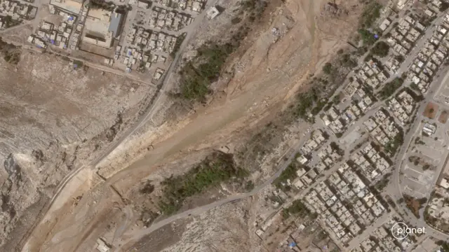 A satellite photo of the collapsed dam, with dozens of buildings either side