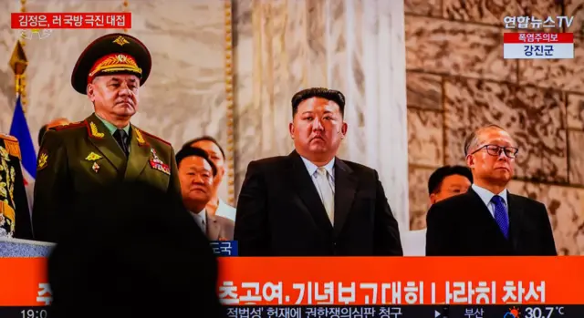 A TV screen shows North Korean leader Kim Jong Un, Russian Defense Minister Sergei Shoigu and Chinese Communist Party politburo member Li Hongzhong watching a military parade