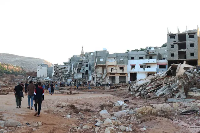 People walk amid rubble and ruined buildings in Derna