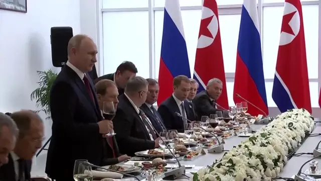 Russia's Vladimir Putin raising his glass at a table to toast North Korea's Kim Jong Un